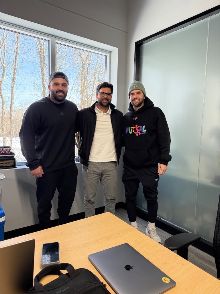 Sam Viana with two colleagues in an office, futsal trophies in the background