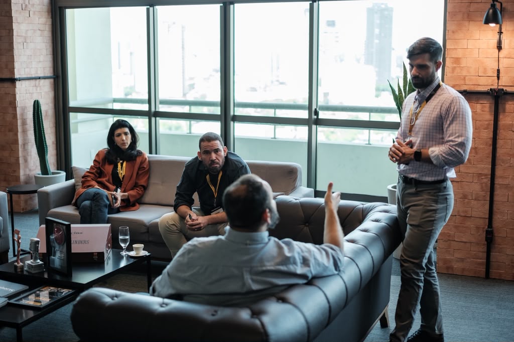 Sam Viana standing while three people sit and talk in a lounge